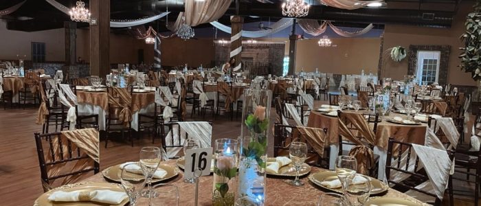 Reception hall at La Hacienda event venue Gainesville GA with gold chargers, champagne napkins, ivory chair sashes, chandeliers, and ceiling drape