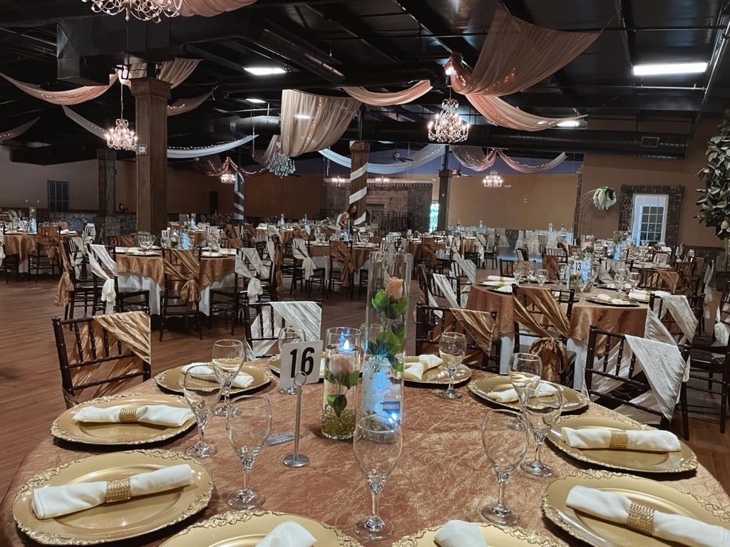 Event Venue Gainesville GA Reception hall at La Hacienda event venue Gainesville GA with gold chargers, champagne napkins, ivory chair sashes, chandeliers, and ceiling drape
